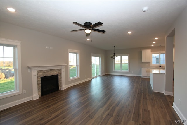 unfurnished living room featuring a stone fireplace, ceiling fan with notable chandelier, a textured ceiling, sink, and dark hardwood / wood-style floors