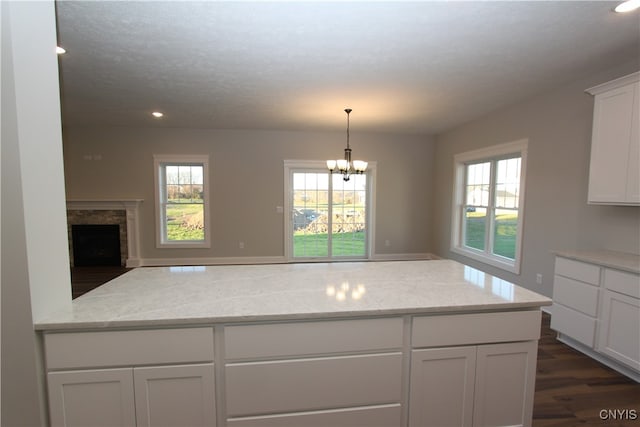 kitchen with white cabinetry, light stone countertops, an inviting chandelier, dark wood-type flooring, and pendant lighting