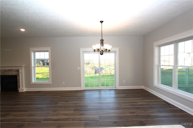 unfurnished living room with a chandelier, plenty of natural light, a textured ceiling, and dark hardwood / wood-style flooring