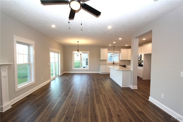 unfurnished living room featuring ceiling fan with notable chandelier, dark wood-type flooring, a textured ceiling, and sink