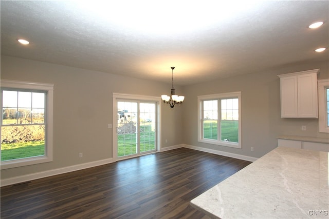 unfurnished dining area with plenty of natural light, dark wood-type flooring, and a notable chandelier