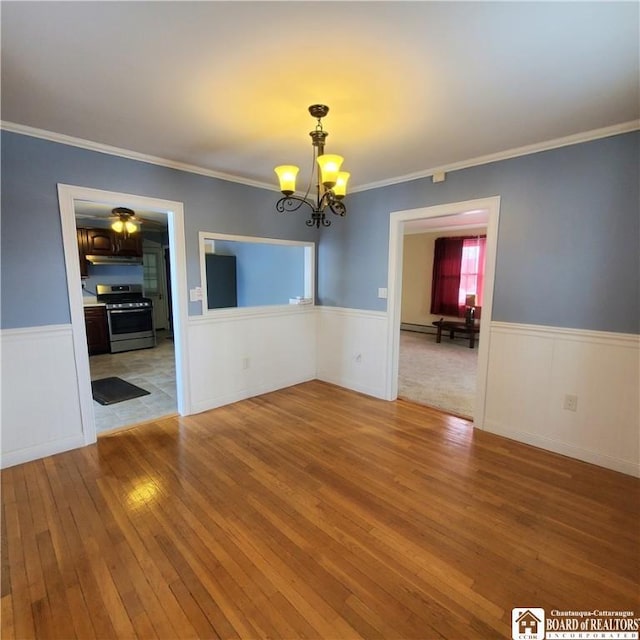 spare room featuring wood-type flooring, ornamental molding, and an inviting chandelier