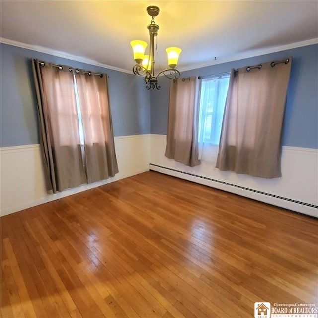 empty room featuring baseboard heating, ornamental molding, a chandelier, and hardwood / wood-style floors