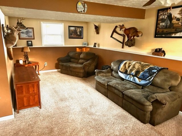 living room featuring ceiling fan, beamed ceiling, a textured ceiling, and carpet floors