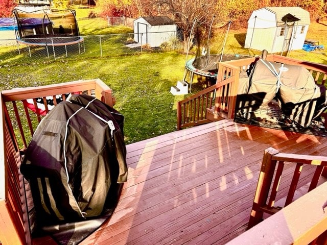 wooden deck featuring a yard, a storage shed, and a trampoline