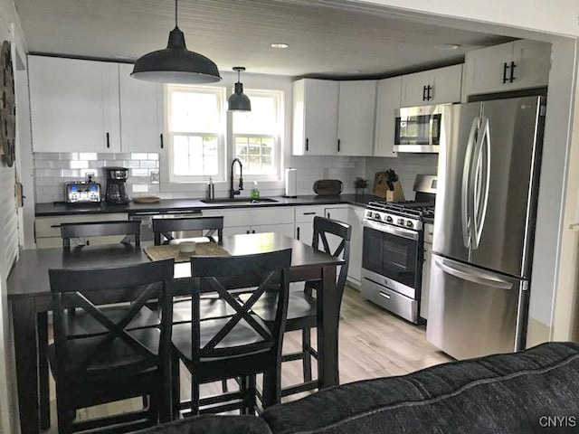 kitchen with tasteful backsplash, appliances with stainless steel finishes, sink, white cabinets, and light hardwood / wood-style flooring