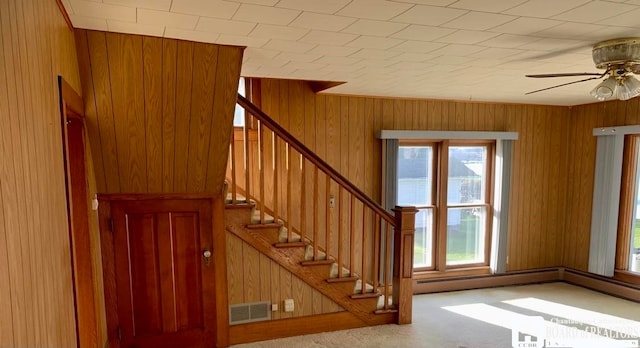 stairs with carpet floors, wooden walls, and ceiling fan