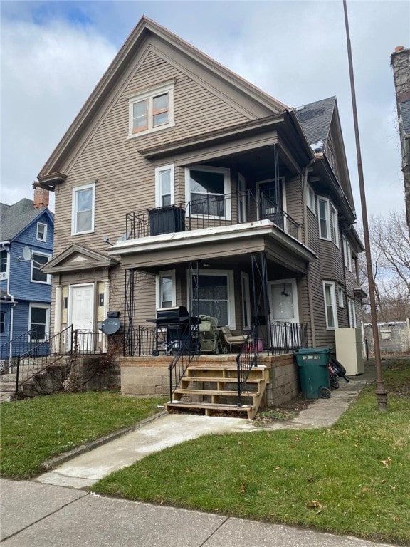 view of front of house with a front yard, a balcony, and covered porch