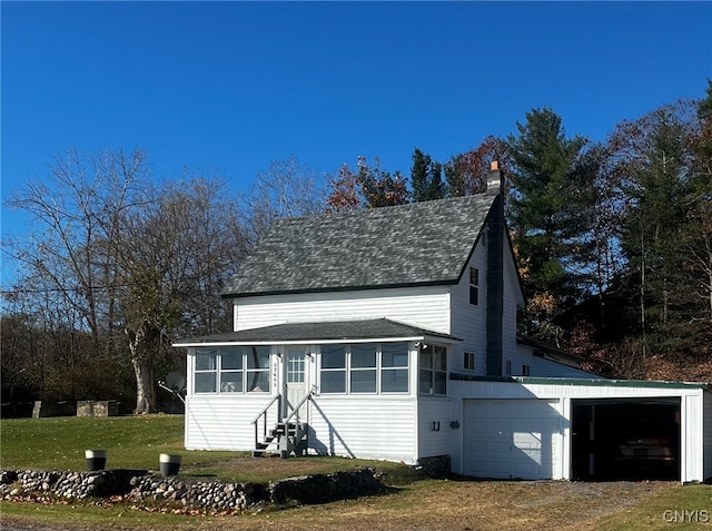 view of outdoor structure with a lawn, a garage, and a sunroom