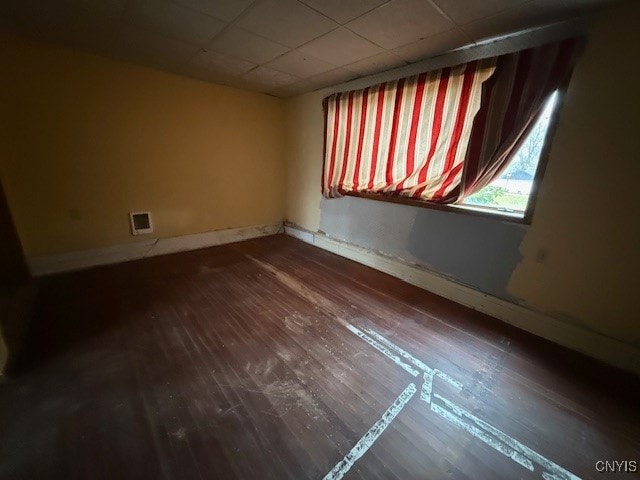 empty room with dark hardwood / wood-style floors and a drop ceiling