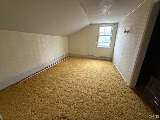 additional living space featuring light colored carpet, wood walls, and vaulted ceiling