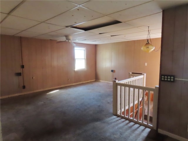 basement featuring ceiling fan, wooden walls, carpet, and a drop ceiling