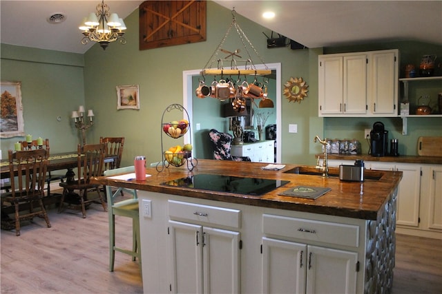 kitchen featuring butcher block counters, light hardwood / wood-style floors, a center island with sink, white cabinets, and black electric stovetop