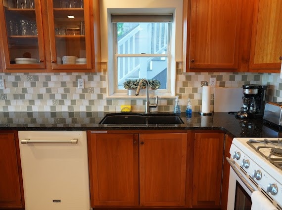 kitchen with dark stone counters, sink, dishwashing machine, and tasteful backsplash