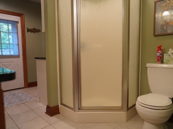 bathroom featuring toilet, an enclosed shower, and tile patterned floors