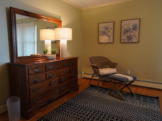 living area with hardwood / wood-style floors, a baseboard heating unit, and crown molding