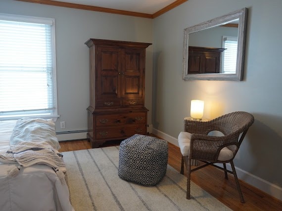 sitting room with baseboard heating, light wood-type flooring, and crown molding