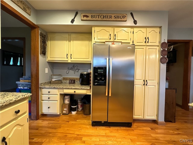 kitchen with stainless steel fridge with ice dispenser, light stone counters, and light hardwood / wood-style flooring