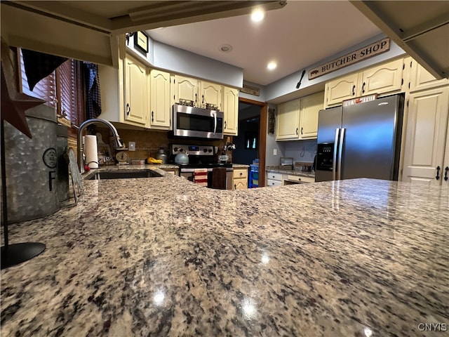 kitchen featuring appliances with stainless steel finishes, stone counters, decorative backsplash, sink, and cream cabinetry