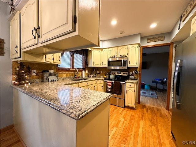 kitchen featuring light wood-type flooring, appliances with stainless steel finishes, light stone countertops, sink, and kitchen peninsula