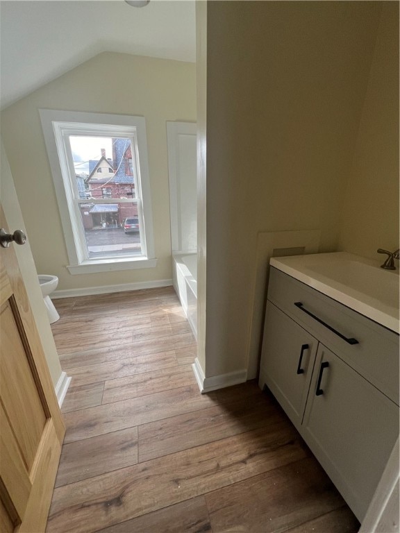 bathroom featuring hardwood / wood-style flooring, vanity, toilet, and vaulted ceiling