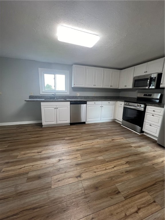 kitchen with dark wood-type flooring, white cabinets, sink, a textured ceiling, and appliances with stainless steel finishes