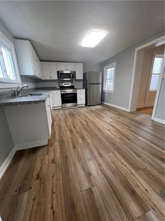 kitchen with stainless steel appliances, light hardwood / wood-style floors, sink, a textured ceiling, and white cabinets