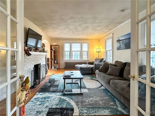 living room featuring hardwood / wood-style floors, ornamental molding, radiator heating unit, and a brick fireplace