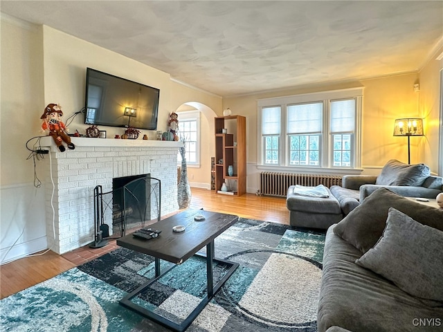 living room featuring a brick fireplace, radiator heating unit, wood-type flooring, and ornamental molding