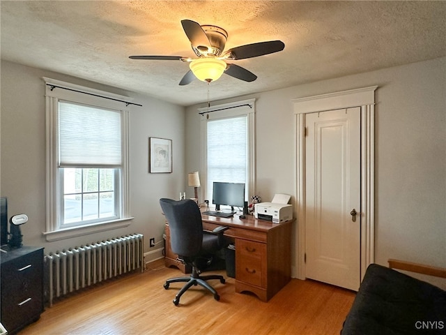 office space featuring radiator, light wood-type flooring, ceiling fan, and a healthy amount of sunlight