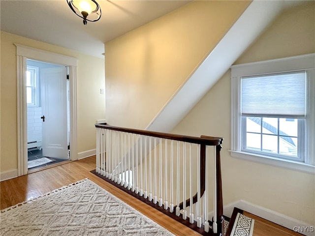 stairs with wood-type flooring, plenty of natural light, and a baseboard heating unit