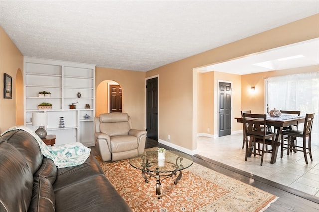 living room featuring built in shelves, a textured ceiling, and light hardwood / wood-style floors