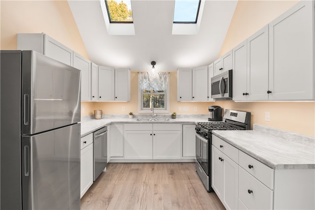 kitchen with stainless steel appliances, vaulted ceiling with skylight, white cabinets, and sink