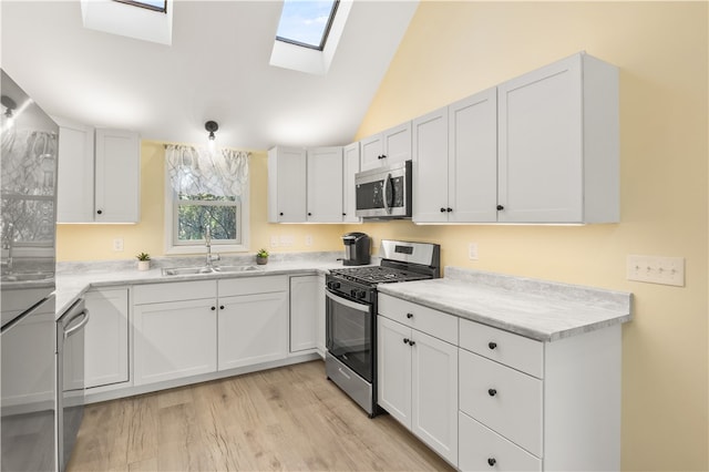 kitchen featuring stainless steel appliances, light hardwood / wood-style floors, sink, vaulted ceiling with skylight, and white cabinets