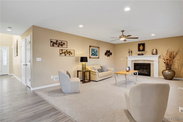 living room with ceiling fan, light hardwood / wood-style floors, and a tiled fireplace