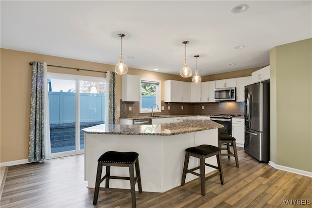 kitchen with hardwood / wood-style flooring, appliances with stainless steel finishes, a kitchen island, white cabinets, and pendant lighting