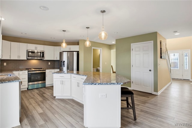 kitchen with a center island, white cabinets, hanging light fixtures, light wood-type flooring, and appliances with stainless steel finishes