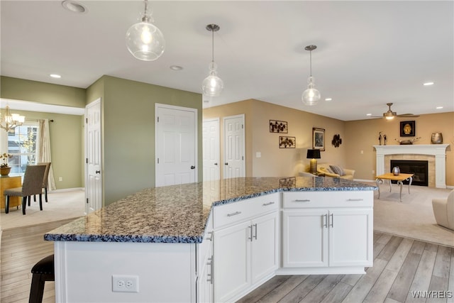 kitchen with light hardwood / wood-style floors, dark stone counters, pendant lighting, a tile fireplace, and white cabinetry