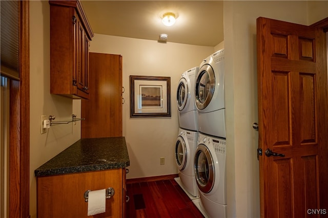 laundry area featuring stacked washing maching and dryer, cabinets, and dark hardwood / wood-style floors