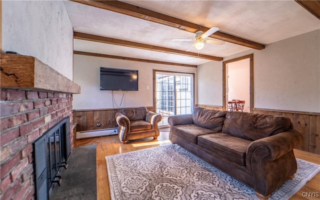 living room with a brick fireplace, ceiling fan, baseboard heating, light hardwood / wood-style flooring, and beamed ceiling