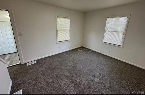 unfurnished room with dark colored carpet and a wealth of natural light