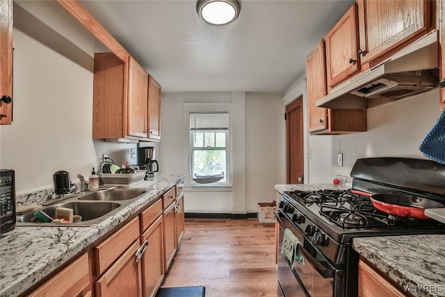 kitchen featuring black range with gas cooktop, sink, light wood-type flooring, and light stone counters