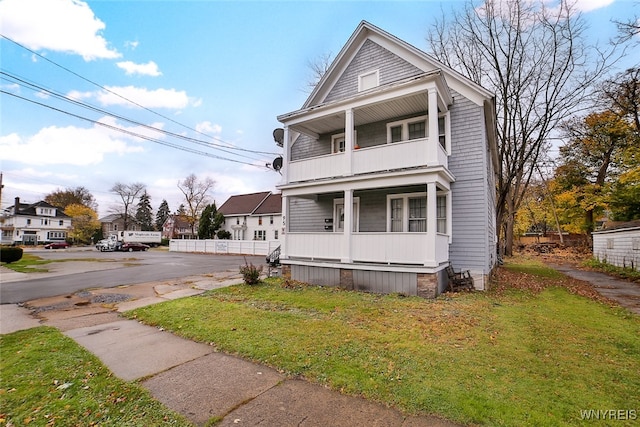 front facade with covered porch, a front yard, and a balcony