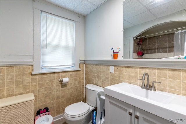 bathroom featuring vanity, a paneled ceiling, toilet, and tile walls