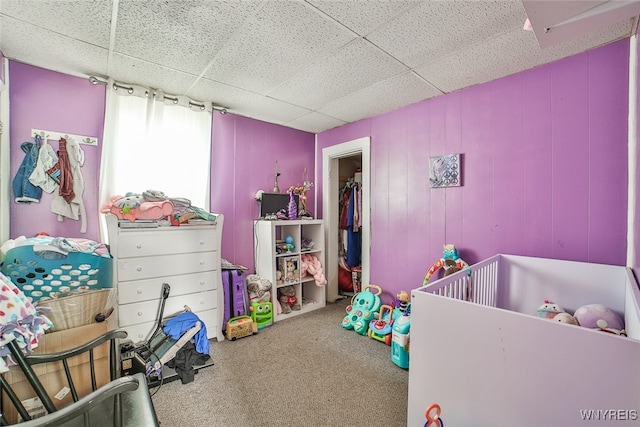 carpeted bedroom with a nursery area and a drop ceiling