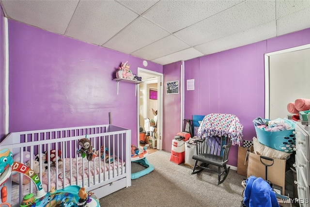 carpeted bedroom with a crib and a paneled ceiling