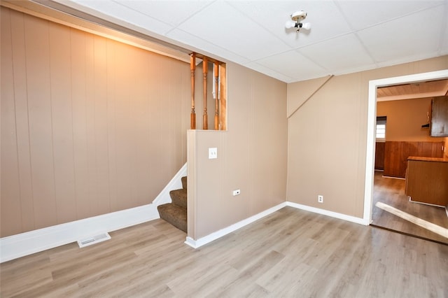 basement with a paneled ceiling, light hardwood / wood-style floors, and wood walls