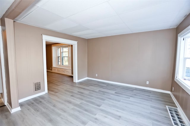 spare room with a drop ceiling and light hardwood / wood-style floors