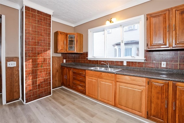 kitchen with dark stone countertops, crown molding, sink, and light hardwood / wood-style flooring