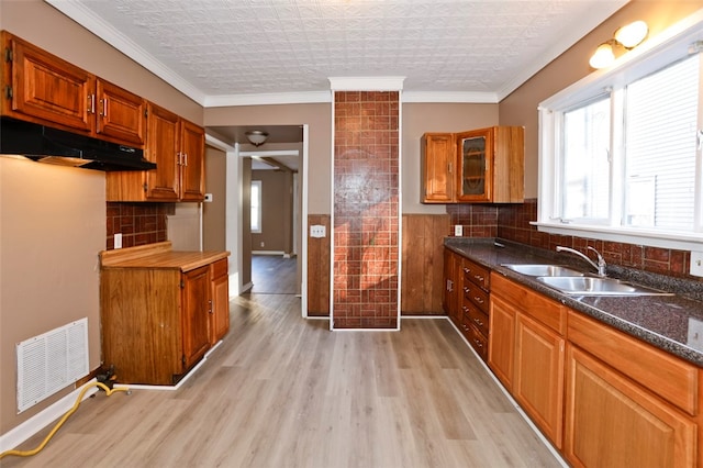 kitchen featuring tasteful backsplash, dark stone counters, ornamental molding, sink, and light hardwood / wood-style flooring